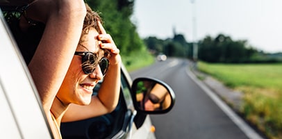 Lachende jonge vrouw kijkt uit open raam van auto