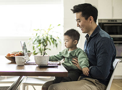 Aziatische man met zoontje op schoot achter laptop