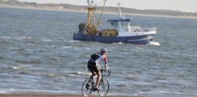 Een vissersboot op zee dicht bij de kust en een fietser op een racefiets