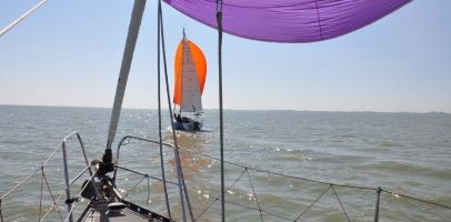 Een afbeelding van een zeilboot op zee met een paarse en oranje zeil. 