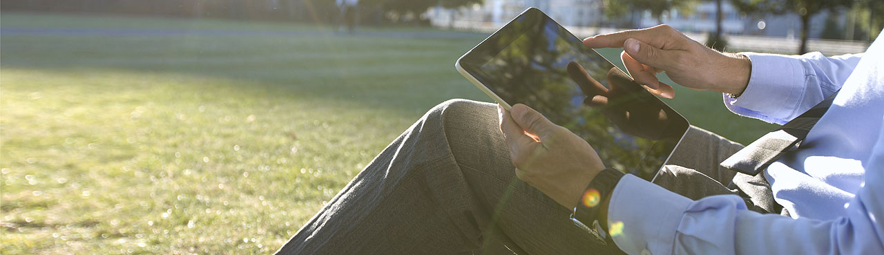 Man zit in het gras en bekijkt NN actualiteiten op tablet